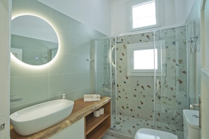 A bathroom with a glass-enclosed shower, a wooden vanity with a sink, and a round mirror.