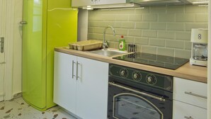 A compact kitchen with white cabinets, a green refrigerator, a stove, and a hanging light fixture. - Aristea in Athens With 2 Bedrooms and 1 Bathrooms (Athens)