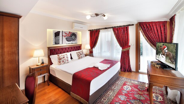 A hotel room with a large bed, a television, a wooden nightstand, a red and white patterned rug, and a red curtain. - Cozy apartment in Old City Center up to 4 people with a Large Terrace (İstanbul)