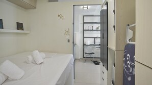 Habitació d'hotel amb llit, una cadira, un armari i una estant amb objectes.
