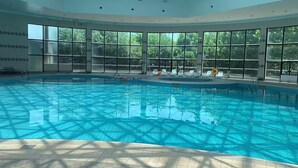 A large indoor swimming pool with clear blue water, surrounded by large windows offering views of greenery. - The Farrington Hotel - Building B (Weifang)