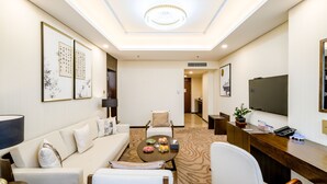 A hotel room with a sofa, armchairs, a coffee table, a desk, and a TV. - The Farrington Hotel - Building B (Weifang)
