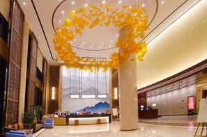 A spacious lobby with a reception desk, a large decorative column, and a mural of mountains on the wall. - The Farrington Hotel - Building B (Weifang)