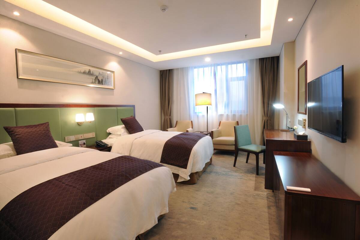 A hotel room with two beds, a desk, a chair, a TV, and a window with curtains.