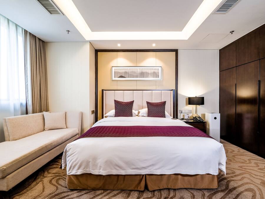 A hotel room with a large bed, a sofa, a desk with a lamp, and a wardrobe.