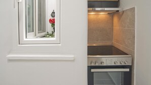 A compact kitchen with a built-in oven, a stove, and a window with a view of red flowers outside. - Sofia s Home in Piraeus (Piraeus)