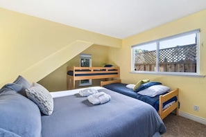 Une chambre avec deux lits, un lit superposé, une fenêtre donnant sur une clôture et un plafond en pente.