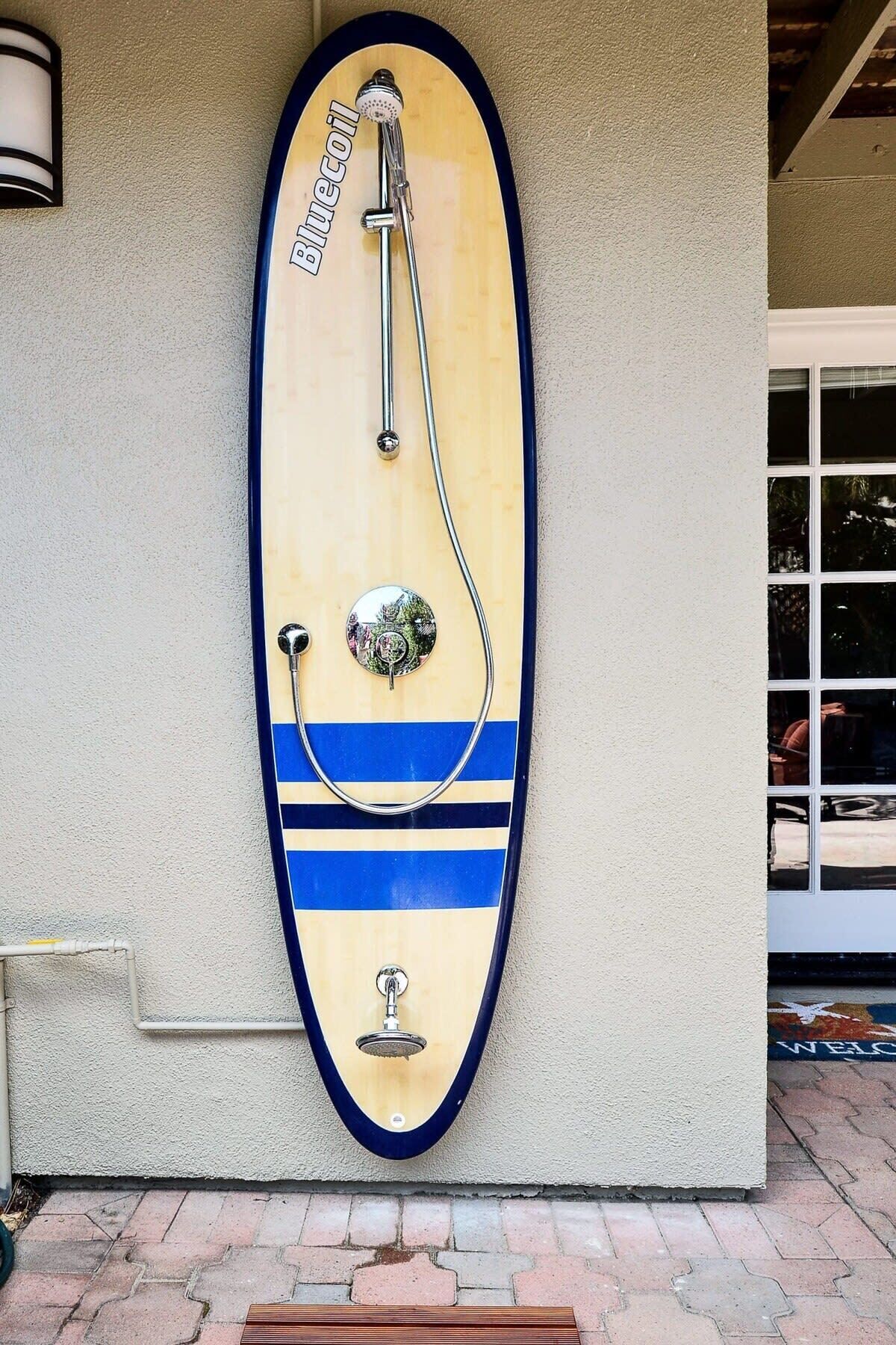 A wall-mounted shower with a surfboard design, a handheld showerhead, and a control knob.