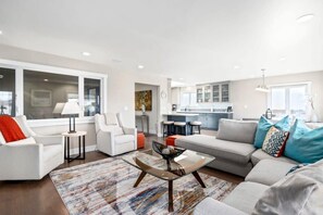 Un salon moderne avec un canapé, des fauteuils, une table basse et une cuisine en arrière-plan.