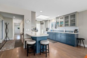 A modern kitchen with a central island, bar stools, and blue cabinetry. - Oceanview Retreat with Hot Tub (Santa Cruz)