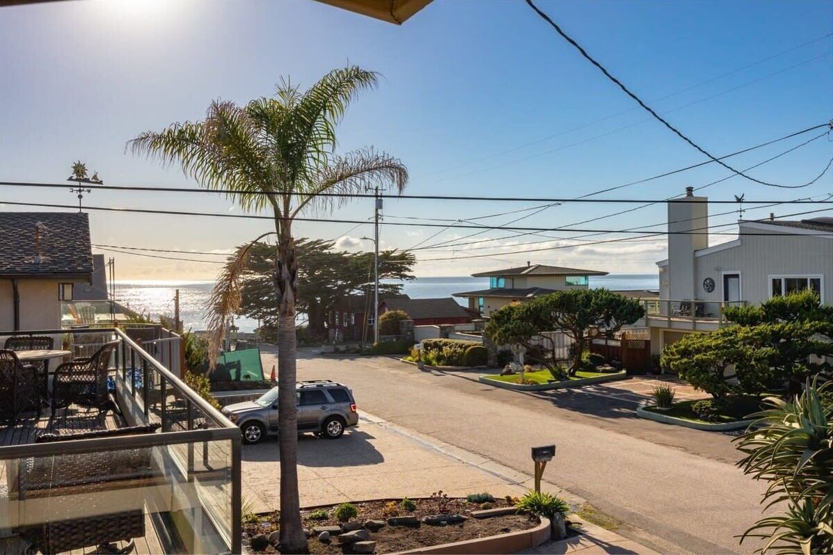 A residential street with houses, a parked car, and a view of the ocean.