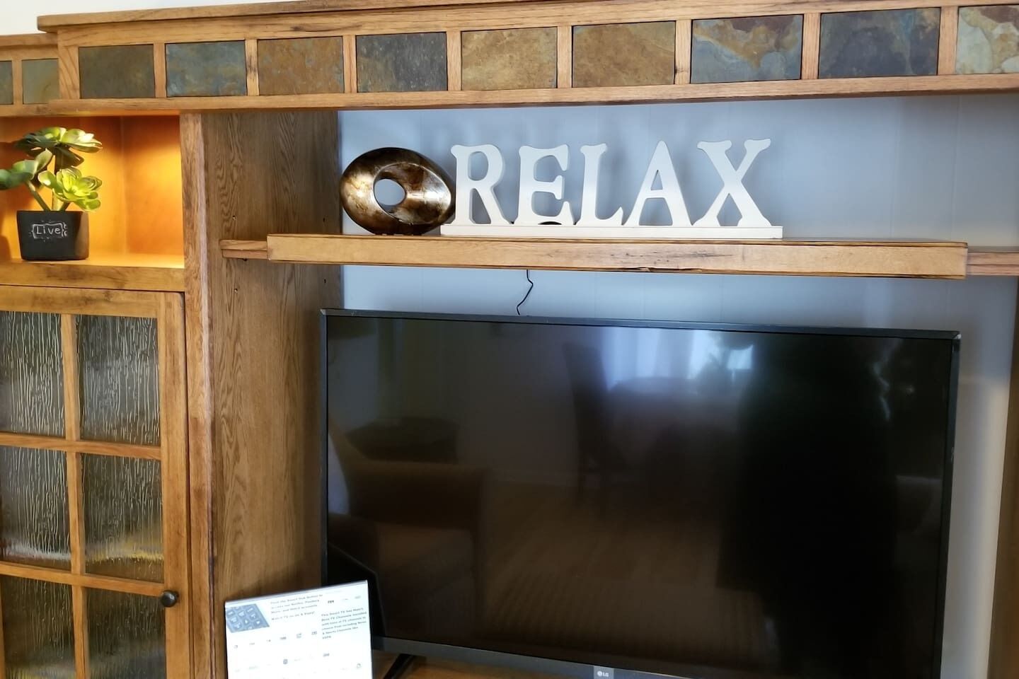 A living room with a TV, a 'RELAX' sign, and a plant on a shelf.