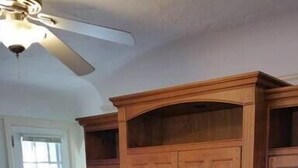Una sala de estar con un mueble de madera, un sofá gris con cojines blancos y un ventilador de techo.