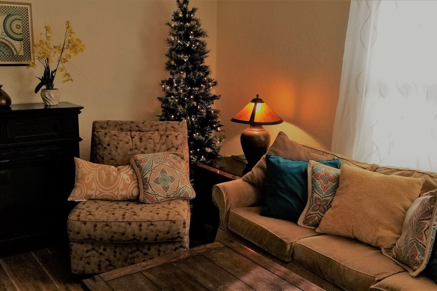 Un salon chaleureux avec un fauteuil à motifs, un canapé agrémenté de coussins décoratifs, une petite table avec une lampe et un sapin de Noël.
