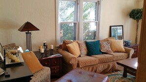 Ein gemütliches Wohnzimmer mit einer Couch, einem Couchtisch, einer Lampe und einem Fenster mit Blick auf Grünfläche.