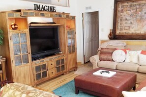 A living room with a wooden entertainment unit, a television, a beige sofa, and a red leather ottoman.