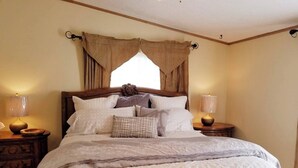 Una cama bien hecha con cabecera de madera, dos mesitas de noche con lámparas y una ventana con cortinas.