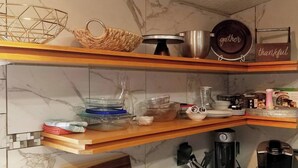 Una cocina con encimeras de mármol, repisas de madera y diversos utensilios, como una cafetera, un hervidor y un molinillo de café.