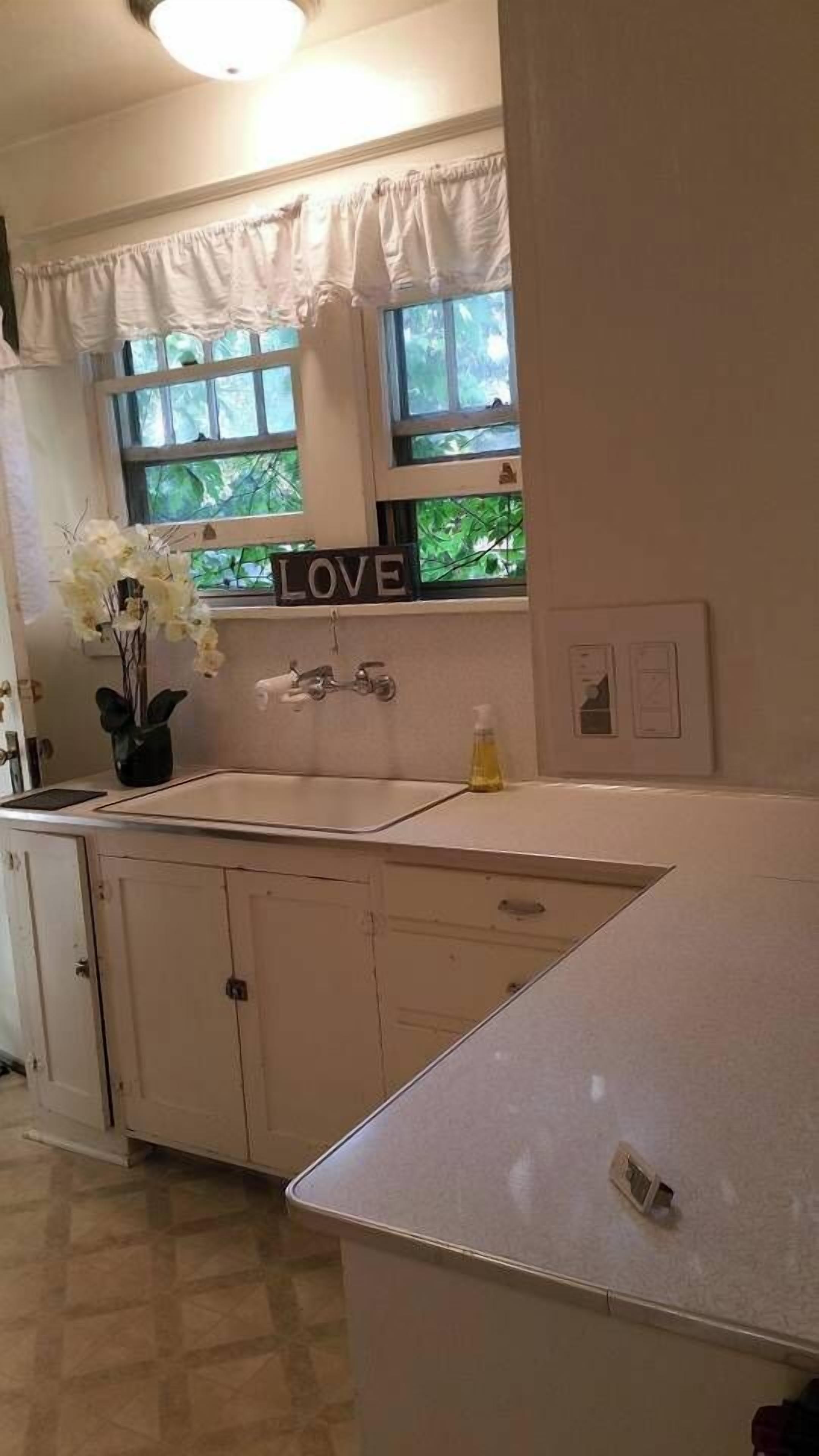 Una cocina con encimera blanca, un lavamanos y un ventanal con un letrero que dice 'LOVE'.