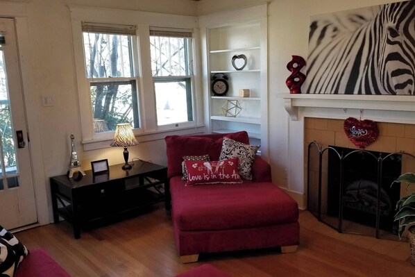 A cozy living room with a red sofa, a small table with a lamp, a fireplace, and a zebra-themed artwork on the wall.