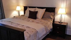 Ein ordentlich bezogenes Bett mit einem floralen Überwurf, zwei Nachttische mit Lampen und ein dunkles Holz-Kopfteil.
