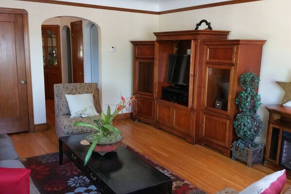 A living room with a floral-patterned sofa, a wooden cabinet with a television, and a decorative plant on a coffee table.