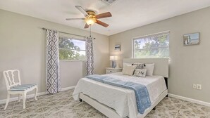 Ein Schlafzimmer mit einem Bett, einem Sessel, einem Deckenventilator und zwei Fenstern.