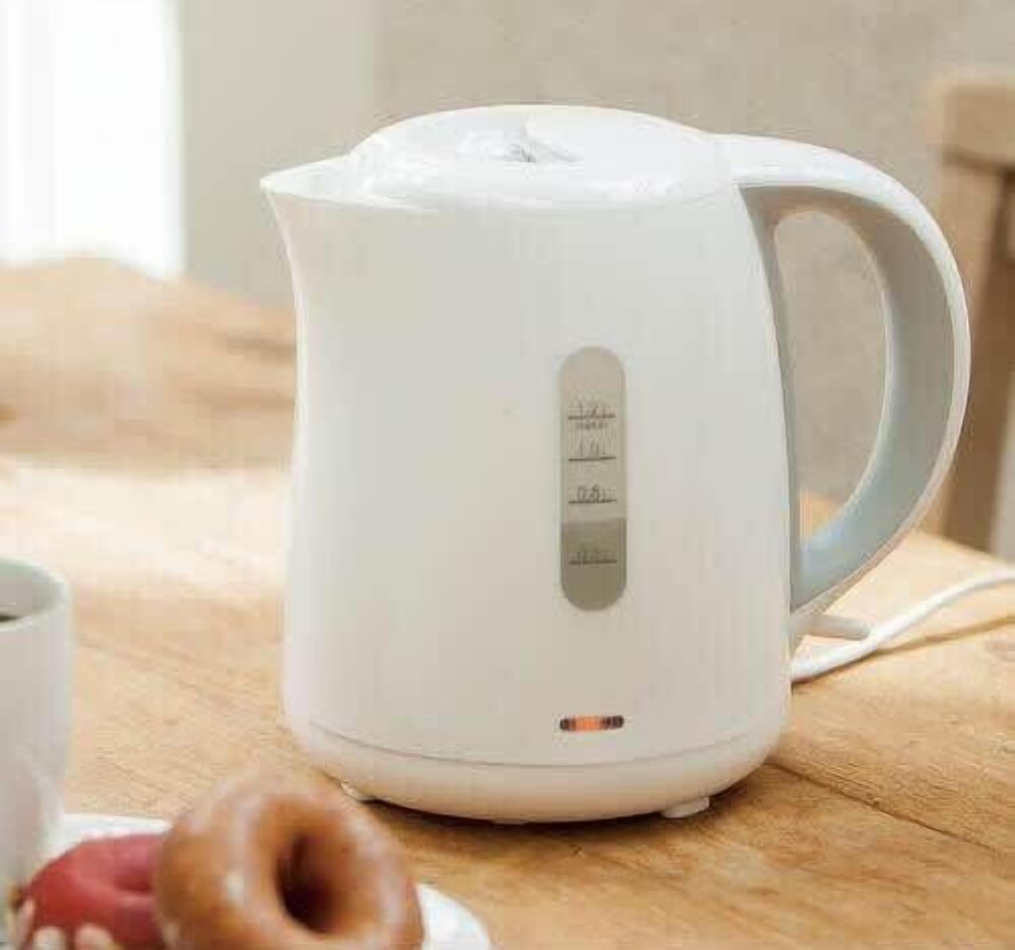 A white electric kettle on a wooden surface with a handle and a control panel with measurement markings.