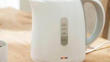 A white electric kettle on a wooden surface with a handle and a control panel with measurement markings.