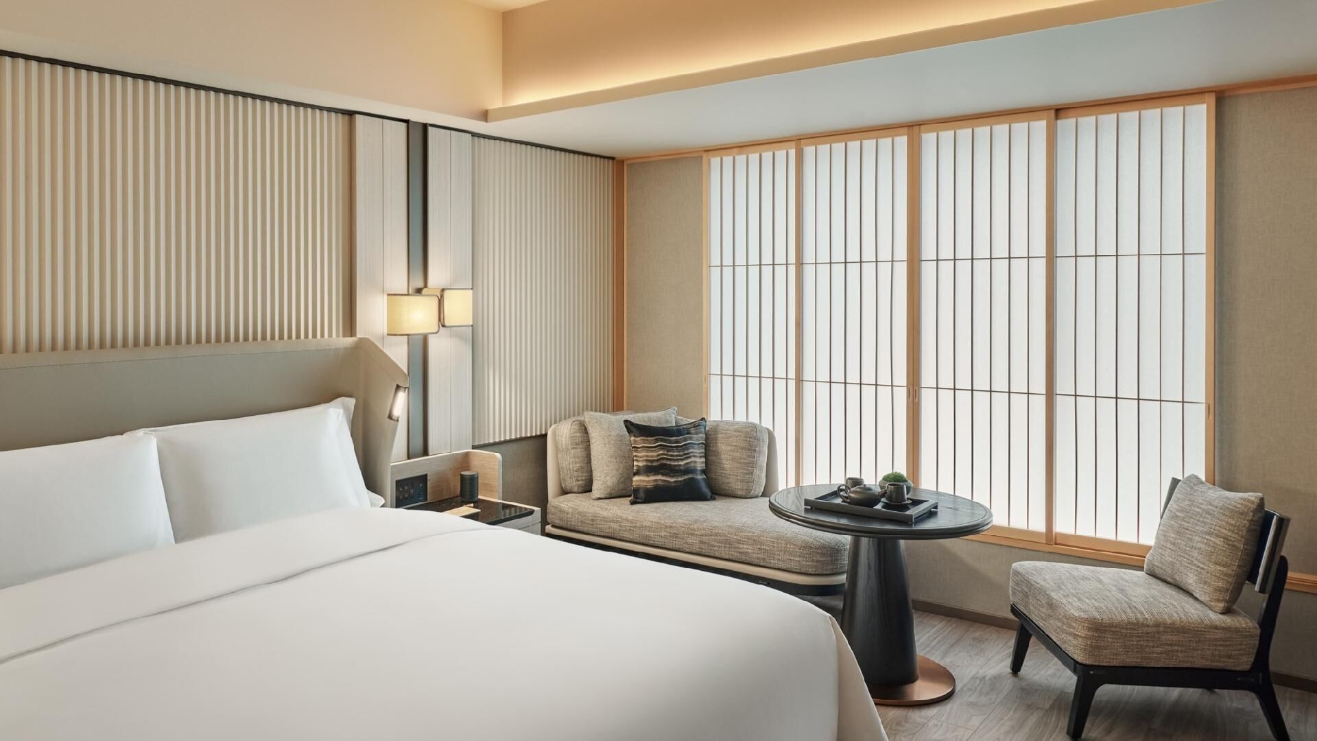 A hotel room with a large bed, a seating area with a table, and a view through shoji screens.