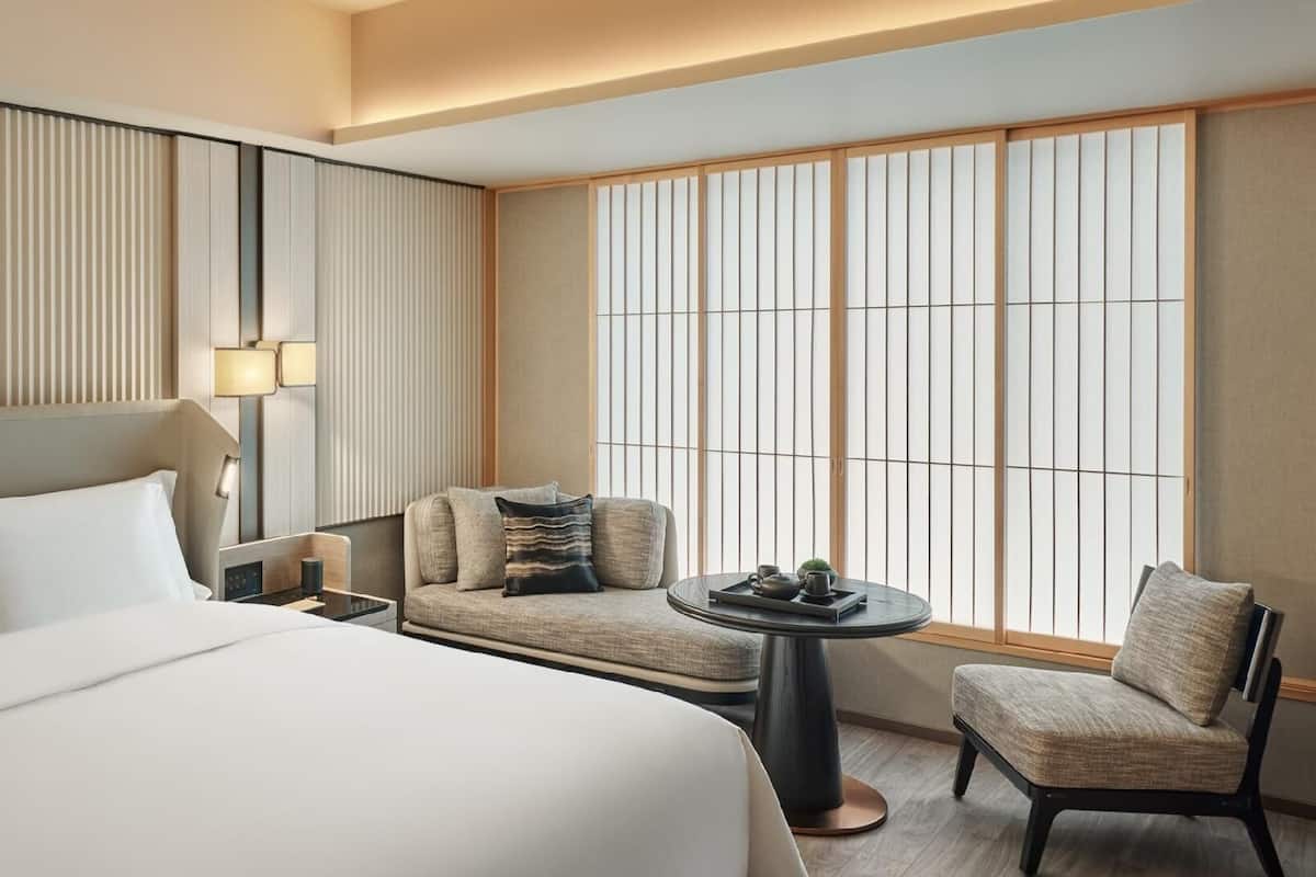 A hotel room with a large bed, a seating area with a table, and a view through shoji screens.