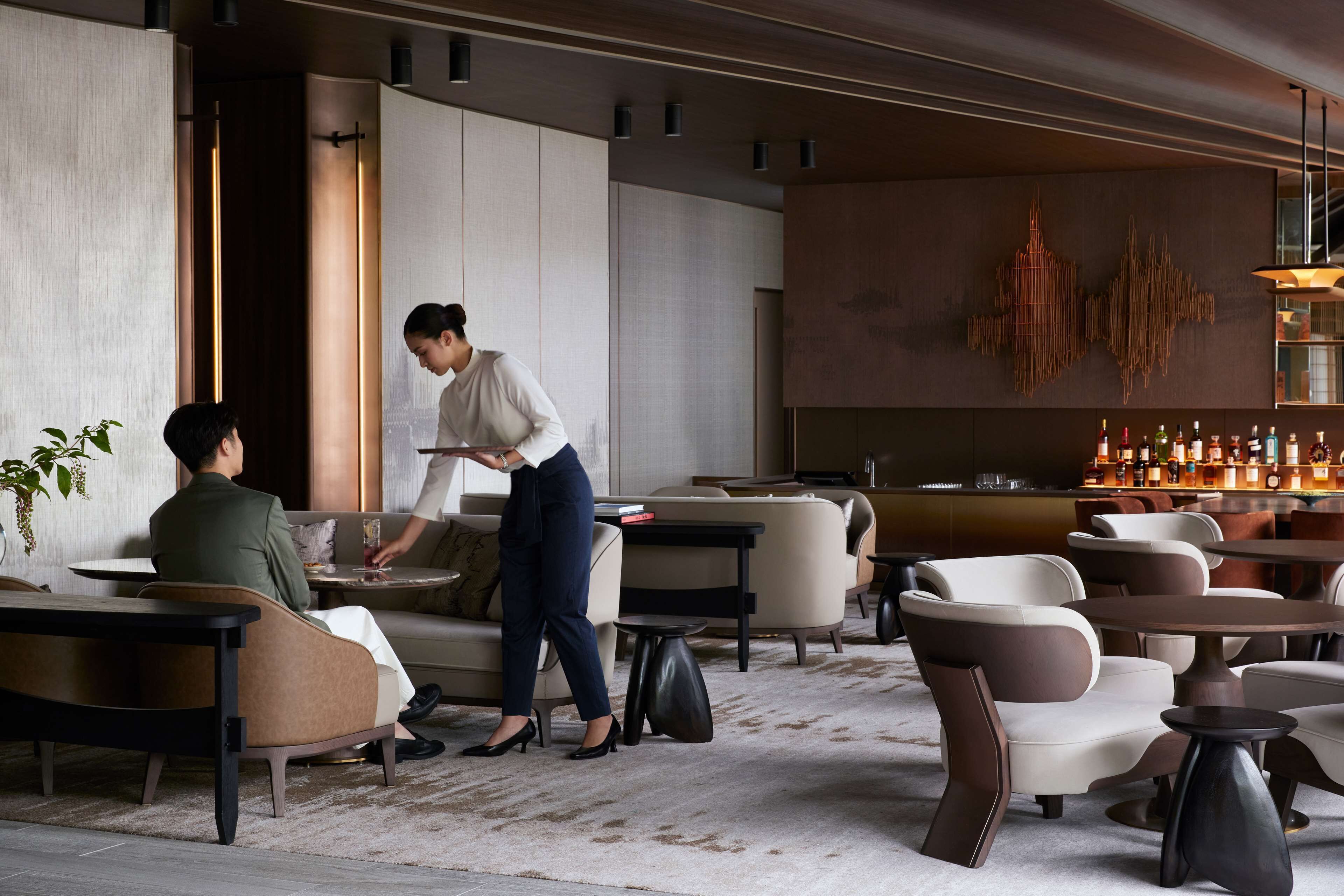 A modern hotel lobby with seating areas, a bar, and a large abstract wall art piece.