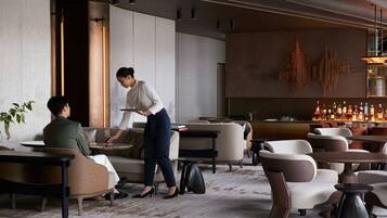 A modern hotel lobby with seating areas, a bar, and a large abstract wall art piece.