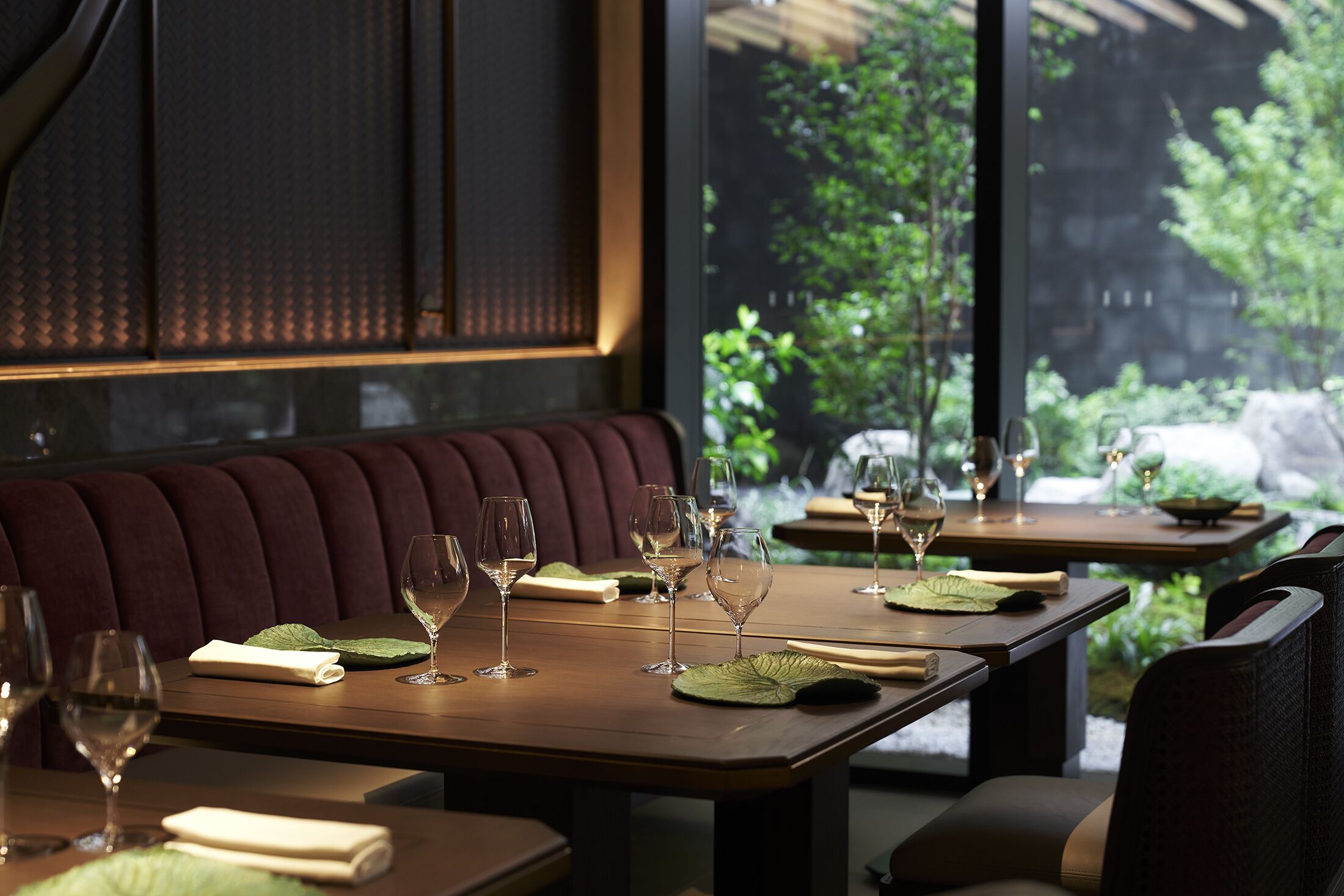 A restaurant with tables set for dining, featuring a view of greenery outside.