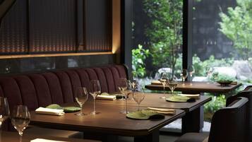A restaurant with tables set for dining, featuring a view of greenery outside.