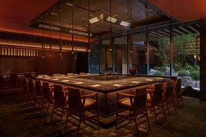 A modern dining area with a central island, multiple chairs, and a view of the outdoors. - Dusit Thani Kyoto (Kyoto)