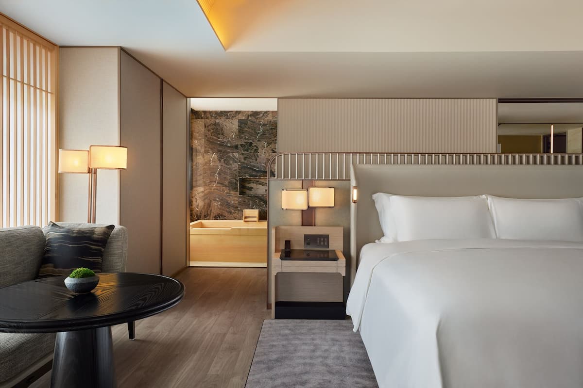 A modern hotel room with a large bed, a small table, a sofa, and a nightstand with lamps.