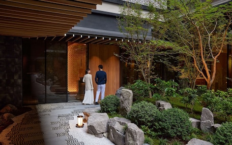 A modern building with a wooden entrance, a garden with rocks and greenery, and a patterned floor.