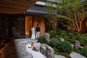 A modern building with a wooden entrance, a garden with rocks and greenery, and a patterned floor. - Dusit Thani Kyoto (Kyoto)