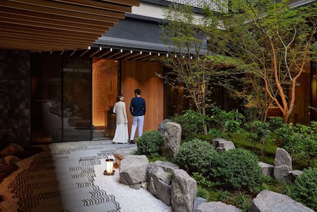 A modern building with a wooden entrance, a garden with rocks and greenery, and a patterned floor.