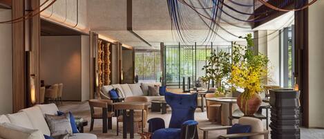 A spacious lounge area with modern furniture, a large window offering a view of greenery, and a unique ceiling design with hanging elements.