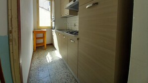 A narrow kitchen with light wooden cabinets, a stainless steel sink, and a window providing natural light. - Tavolini 4 Apartment (Florence)