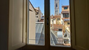 A view through a window of a building with a tower and terracotta-tiled roofs. - Tavolini 4 Apartment (Florence)