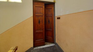 A hallway with two wooden doors, a tiled floor, and a wall with a light switch and a small sign. - Tavolini 4 Apartment (Florence)