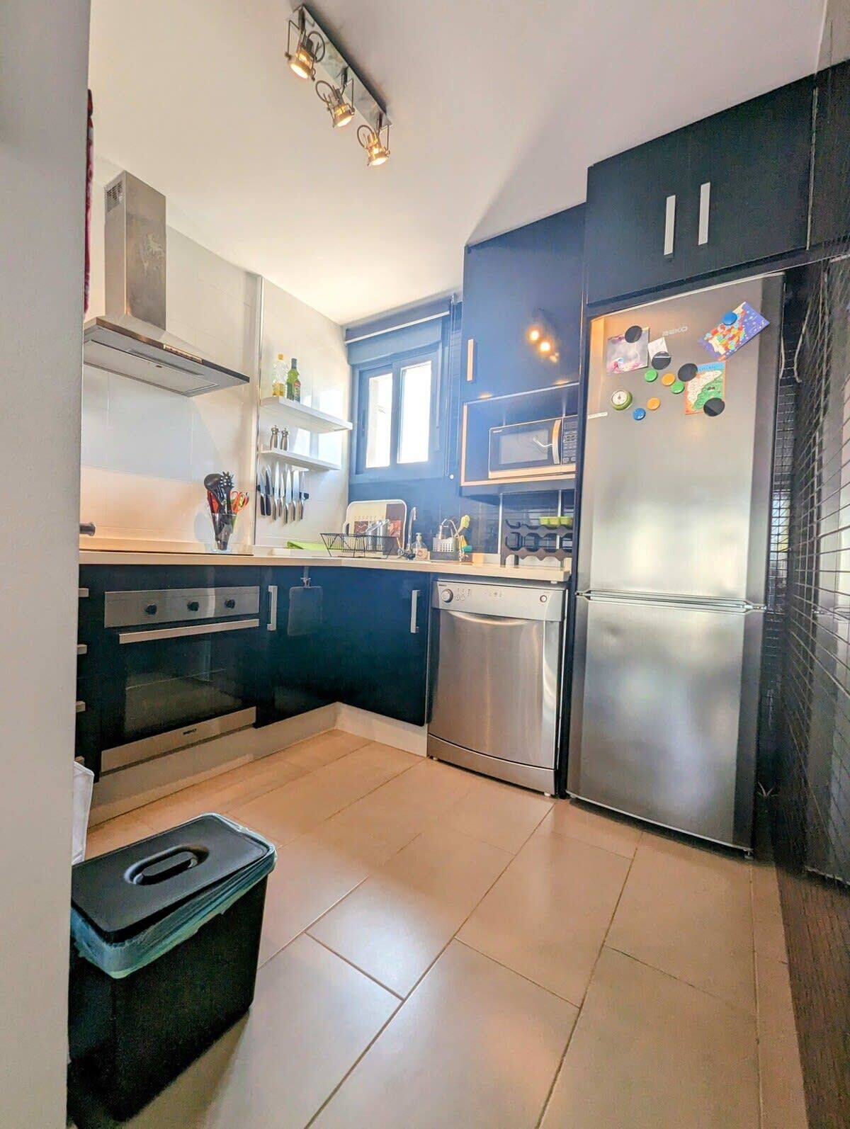 Une cuisine moderne avec des meubles de couleur sombre, des appareils électroménagers en acier inoxydable et un sol carrelé.
