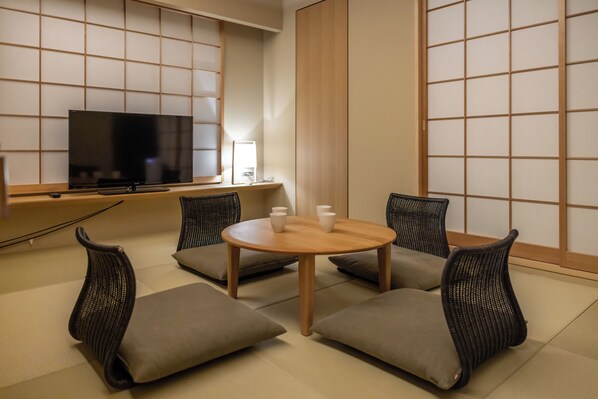 A room with tatami flooring, a television, a round table with chairs, and a sliding door.