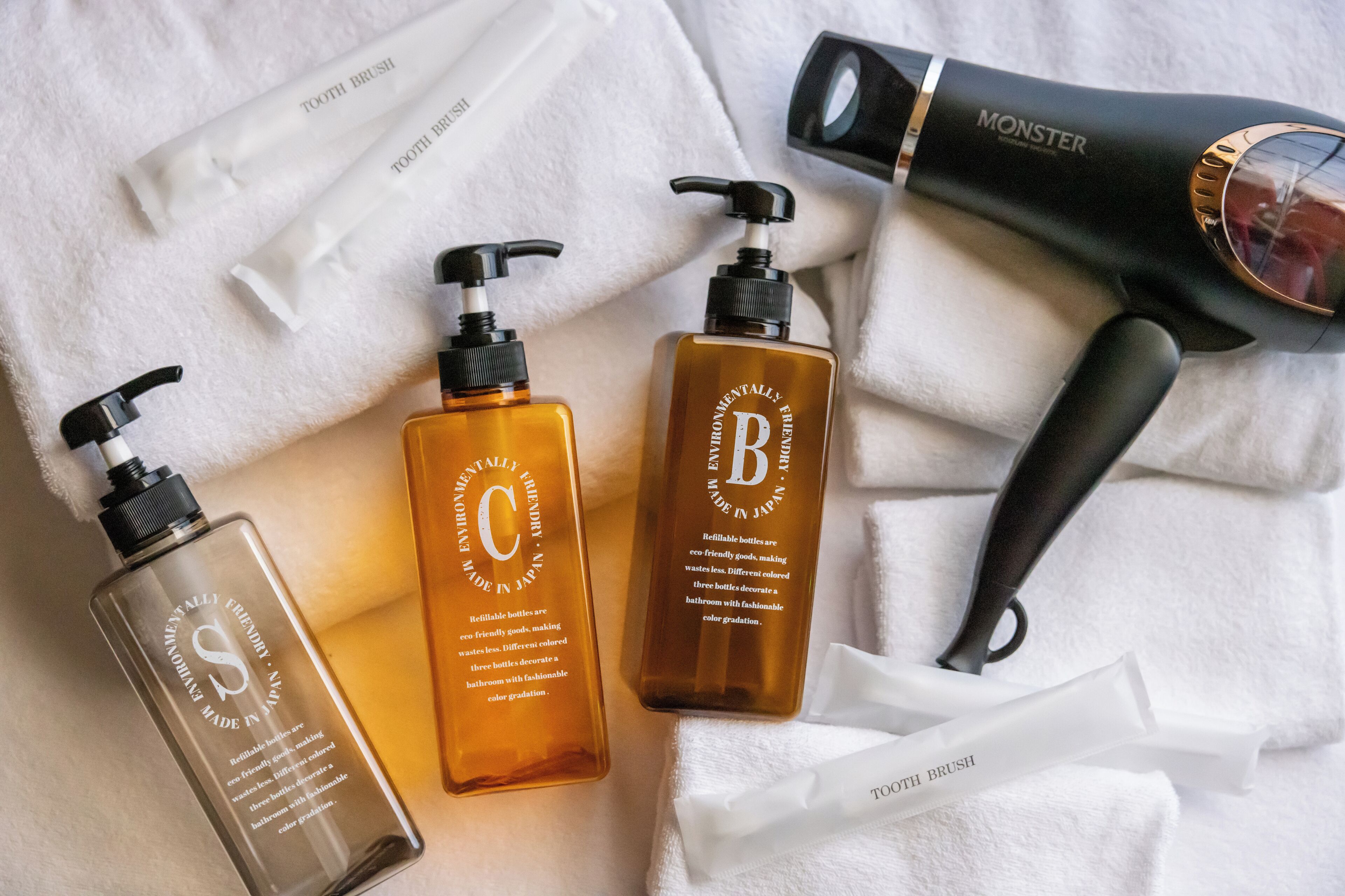 Three bottles of hair care products, a hairdryer, and a white towel on a white surface.