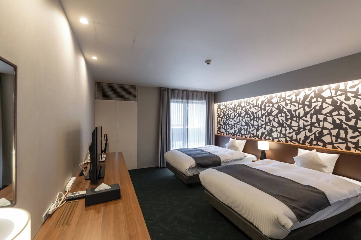 Une chambre d’hôtel avec deux lits, un bureau équipé d’un ordinateur et d’un téléphone, une télévision et un grand mur décoré de motifs.