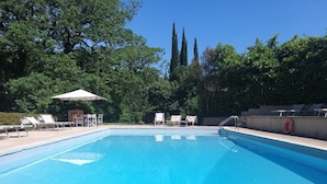 A rectangular swimming pool with clear blue water, surrounded by lounge chairs and a covered seating area. - Castello di Montalto - La Scuola (Castelnuovo Berardenga)