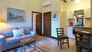 A living room with a sofa, a small table, and a chair. There is a kitchen area with a stove and cabinets. - Castello di Montalto - La Scuola (Castelnuovo Berardenga)